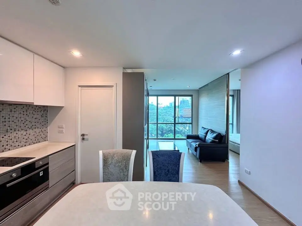 Modern open-layout living room with kitchen and city view, featuring sleek furniture and natural light.