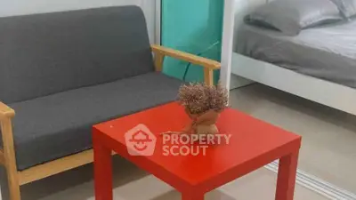 Cozy living area with modern sofa and vibrant red table, adjacent to a comfortable bedroom.