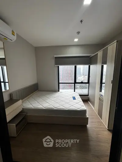 Modern bedroom with city view, featuring a large window and sleek furnishings.