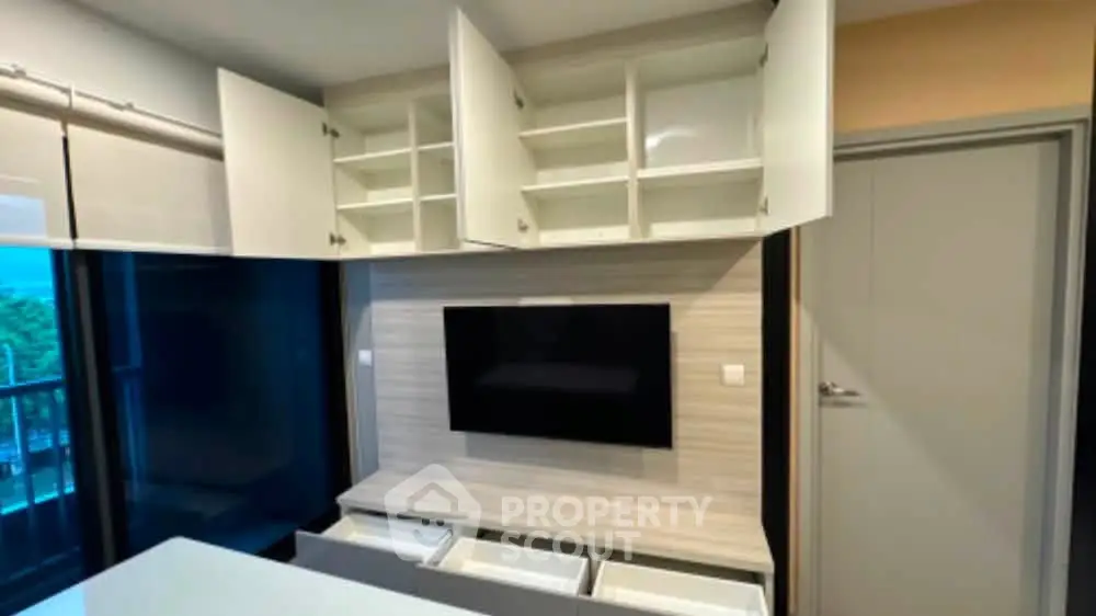 Modern living room with built-in storage and wall-mounted TV, featuring sleek cabinetry and a balcony view.