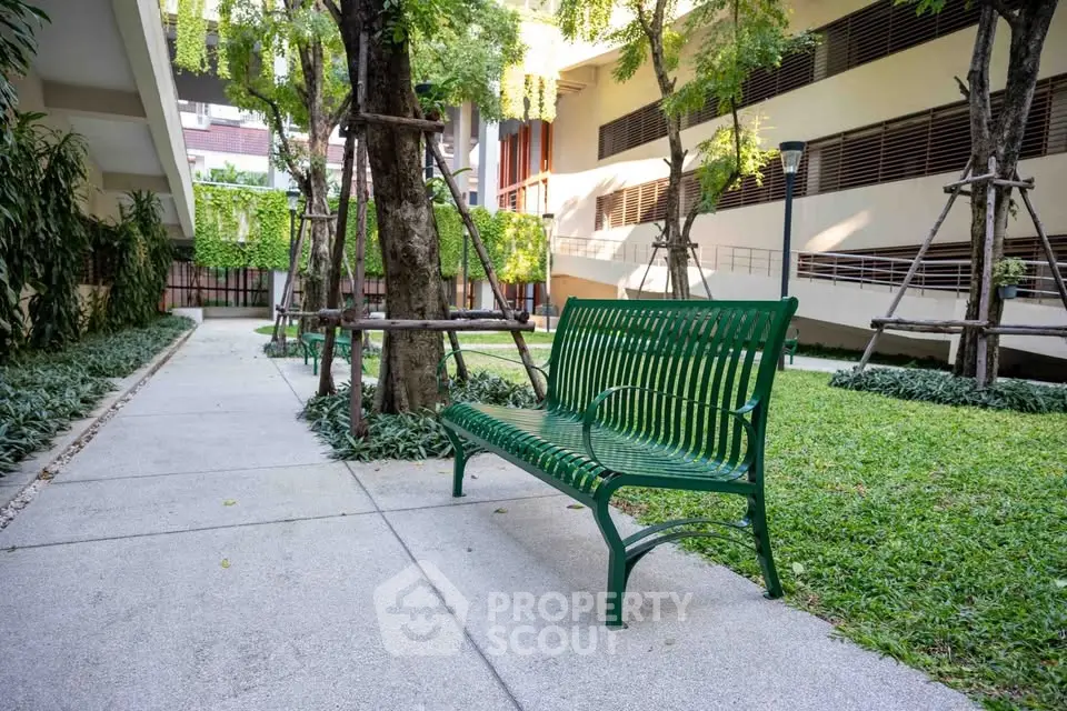 Serene garden area with green bench and lush trees in modern residential complex.