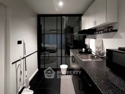 Modern kitchen with sleek black countertops and open layout leading to a cozy bedroom.