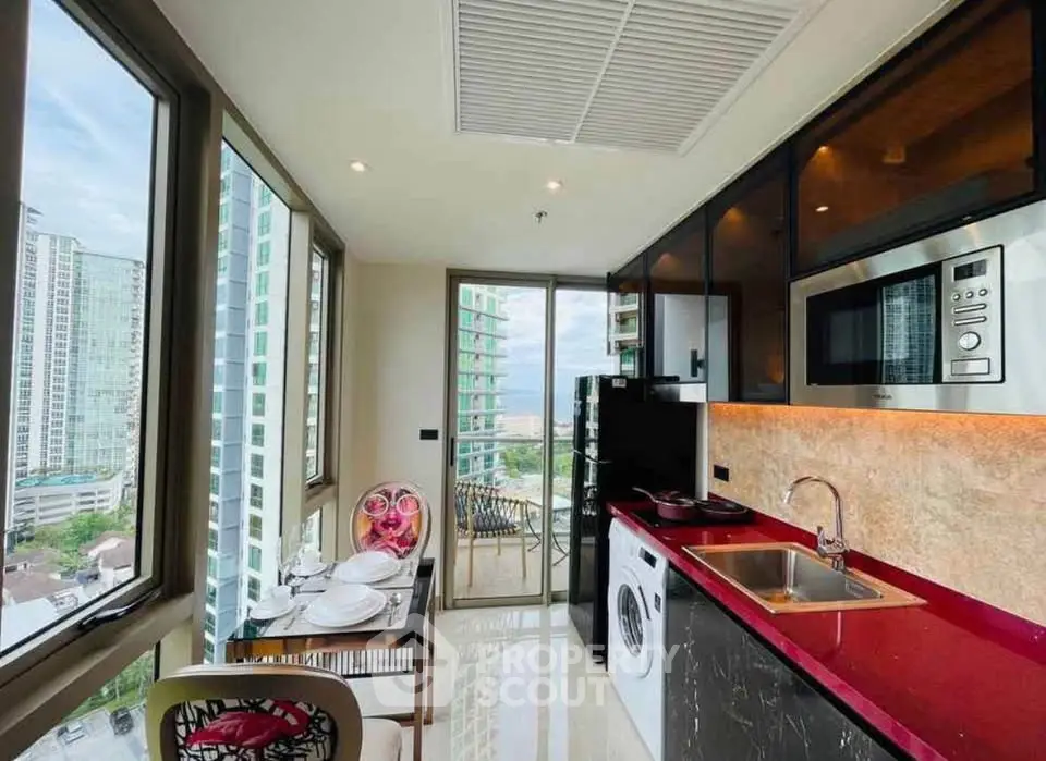 Modern kitchen with red countertops, washing machine, and city view from balcony.