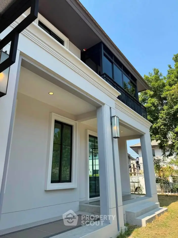 Modern two-story house with sleek design and large windows, surrounded by lush greenery and clear blue sky.