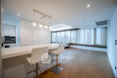 Spacious modern living room with open kitchen and stylish bar stools, featuring large windows and elegant flooring.