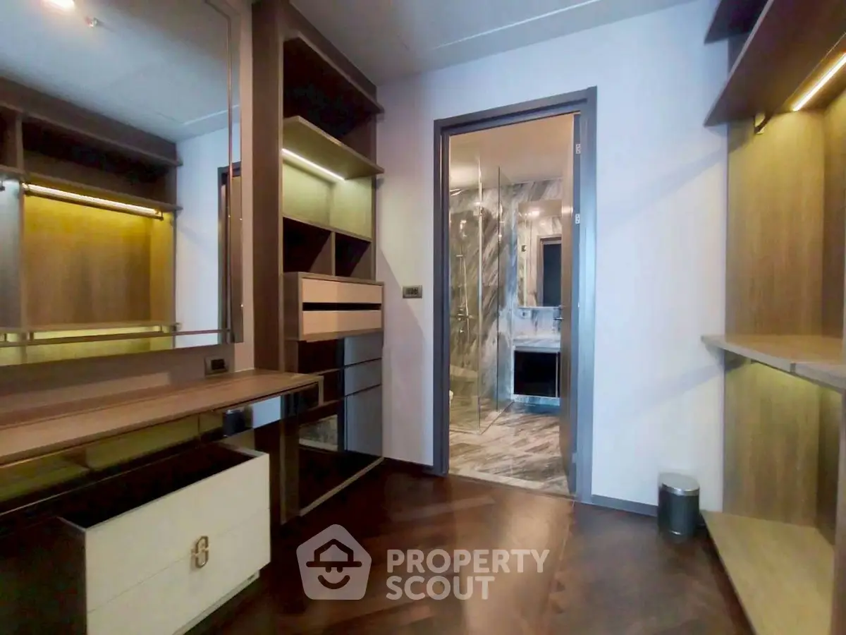 Luxurious walk-in closet with elegant wooden finishes and a view into a marble bathroom.