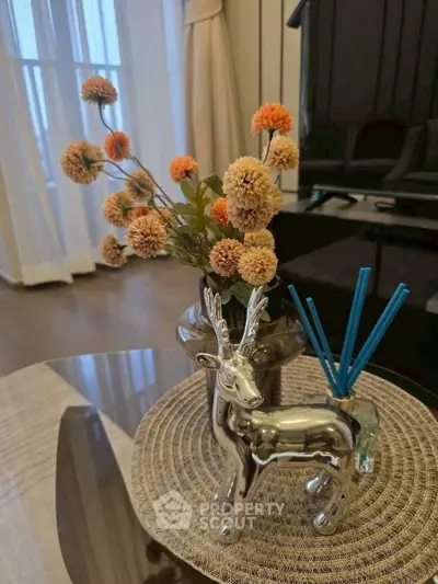 Elegant living room decor with floral arrangement and silver deer figurine on glass table.