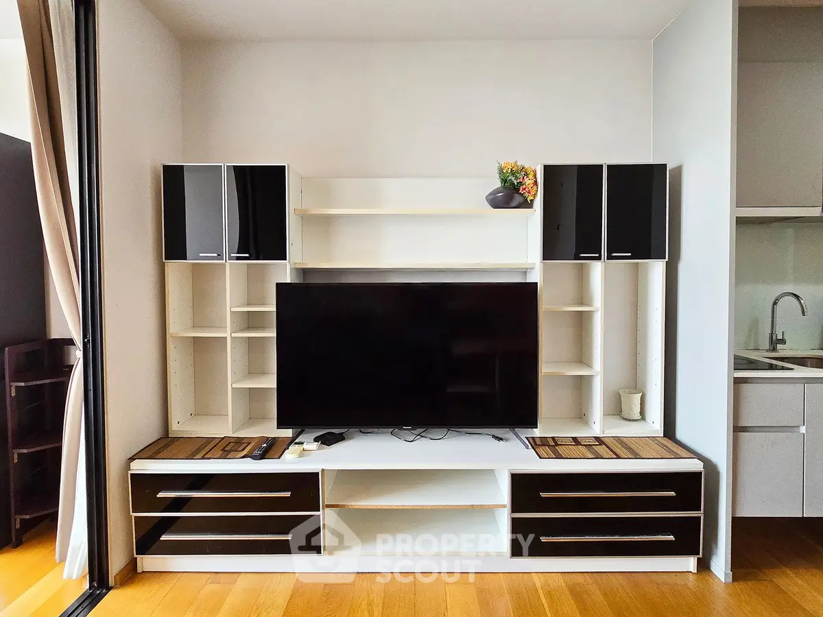 Modern living room with sleek entertainment center and flat-screen TV, adjacent to a compact kitchen area.