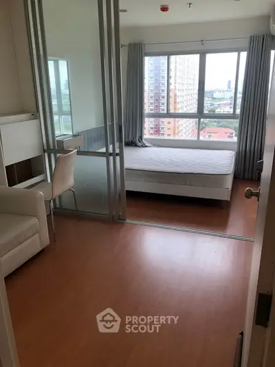 Modern apartment bedroom with large window and city view, featuring sleek furniture and wooden flooring.