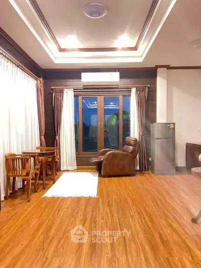 Spacious living room with elegant wooden flooring and modern furniture, featuring a cozy seating area and large windows.