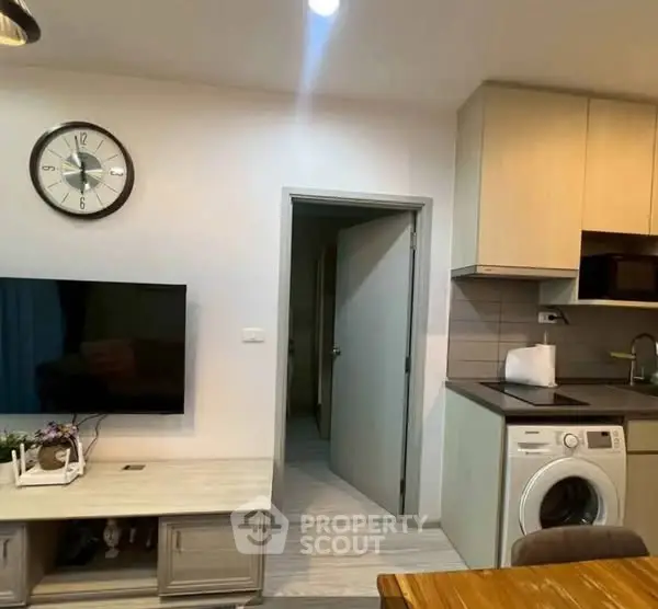 Modern apartment interior with TV, washing machine, and stylish kitchen area.