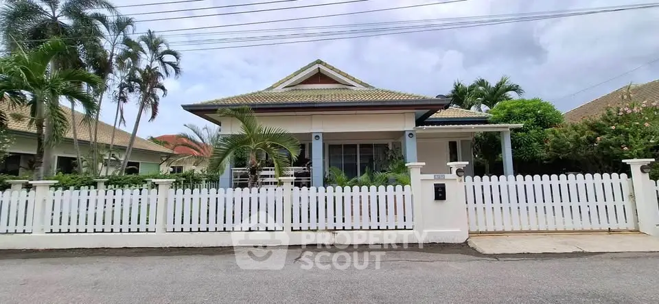 Charming single-story house with white picket fence and lush tropical landscaping.