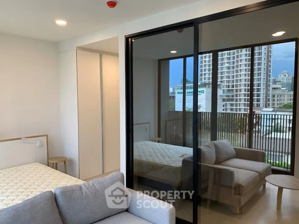 Modern apartment interior with cozy living area and bedroom, featuring large windows and city view.