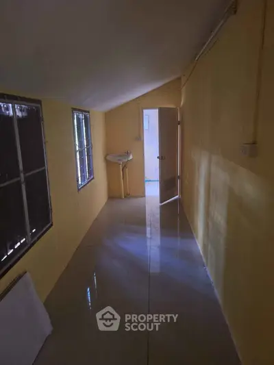 Narrow hallway with yellow walls and a small sink, leading to an open door.