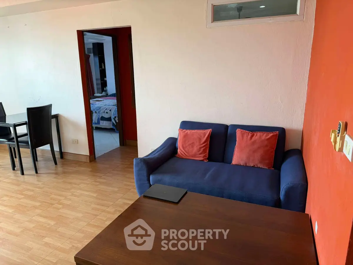 Cozy living room with blue sofa and wooden flooring, adjacent to dining area and bedroom.