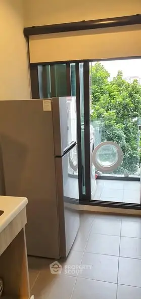 Modern kitchen with fridge and balcony view, featuring lush greenery outside.