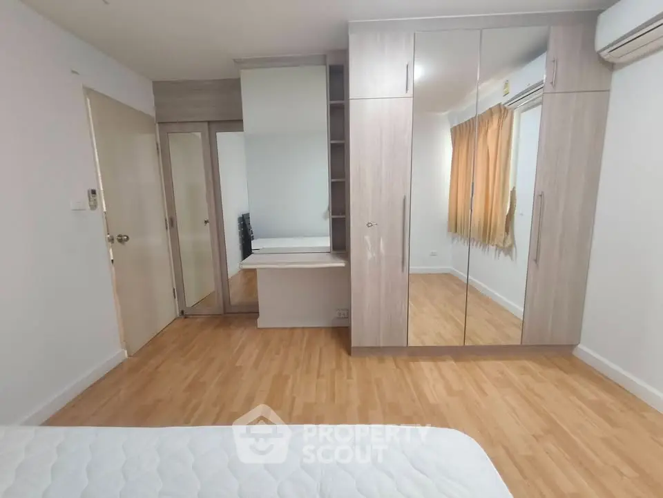 Spacious bedroom with mirrored wardrobe and wooden flooring in modern apartment.