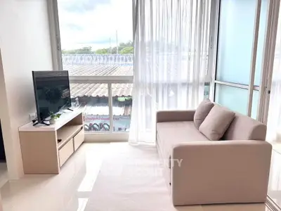 Bright living room with modern sofa and TV, large windows offering natural light and outdoor view.