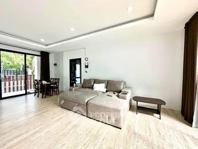 Spacious living room with modern sofa and dining area, featuring large windows and natural light.