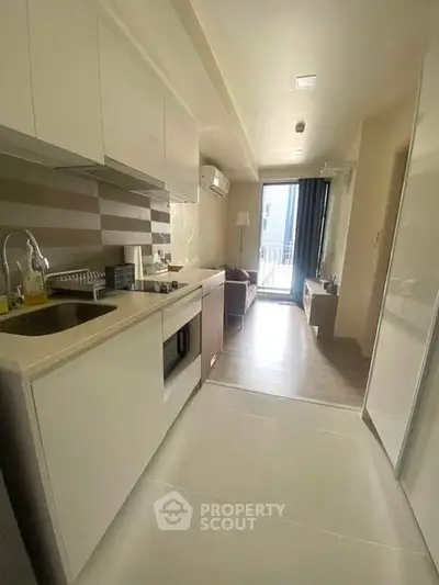 Modern kitchen with sleek cabinetry and open layout leading to a bright living area with balcony access.