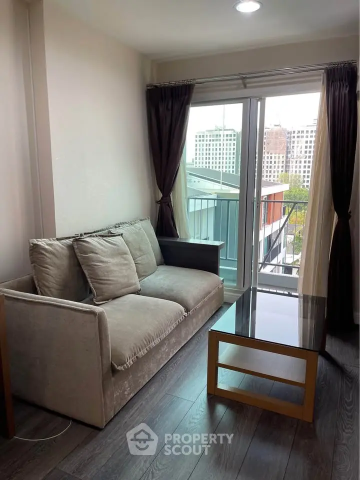 Cozy living room with modern sofa and glass coffee table, featuring a balcony view of the cityscape.