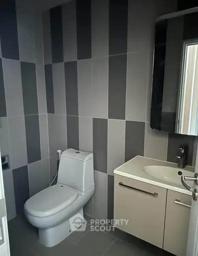 Modern bathroom with sleek design and stylish tiles, featuring a compact toilet and contemporary sink.