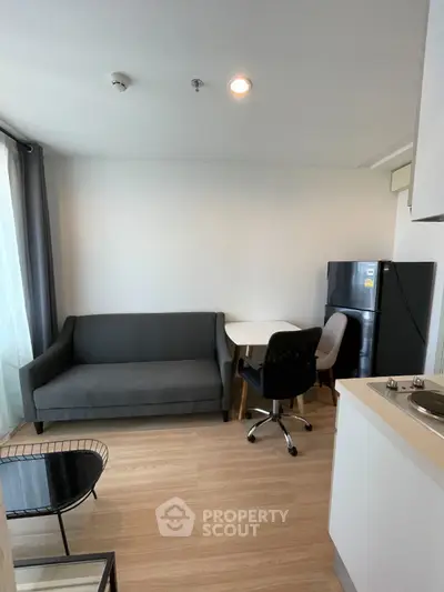 Modern living room with sleek sofa, dining table, and compact kitchen in open layout apartment.