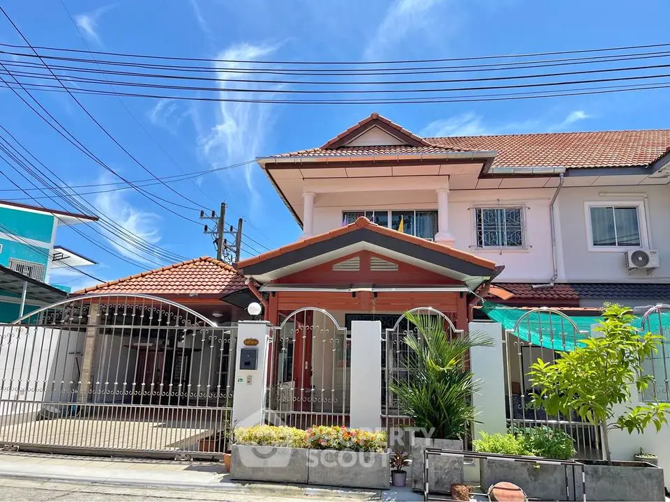 Charming two-story house with red-tiled roof and gated entrance in sunny neighborhood.