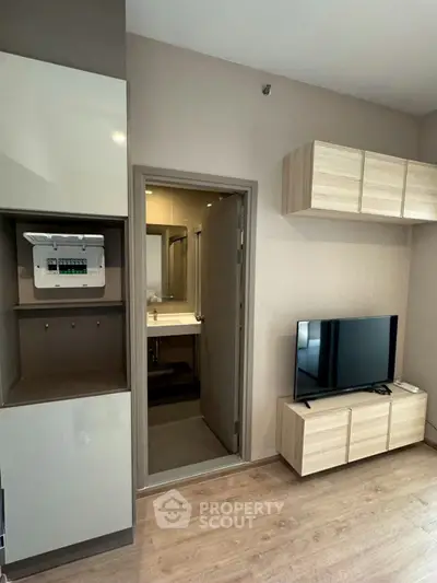 Modern living room with TV and stylish storage cabinets, featuring a glimpse into a sleek bathroom.
