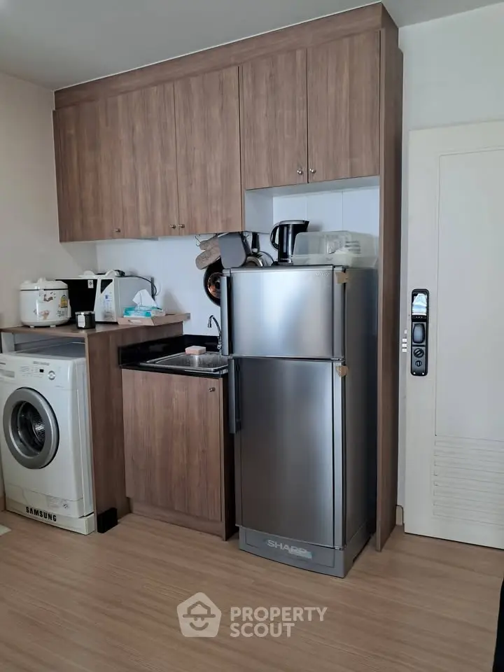 Modern kitchen with wooden cabinets, stainless steel fridge, and washing machine in compact layout.