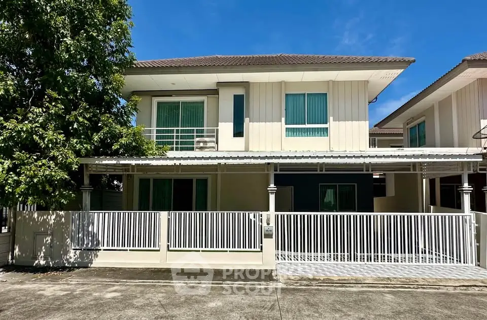 Modern two-story house with white fence and large windows under clear blue sky.