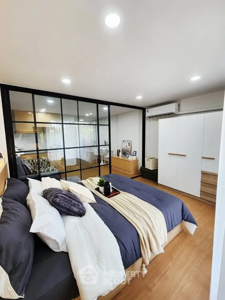 Modern bedroom with stylish decor and mirrored closet doors, featuring cozy bedding and wooden flooring.
