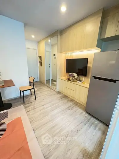 Modern living room with sleek wooden cabinetry and integrated TV, featuring a cozy dining area and stainless steel fridge.