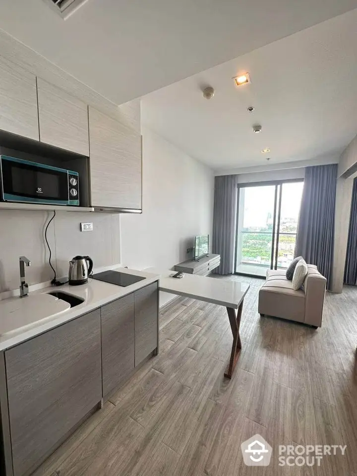 Modern open-plan living room with kitchen, featuring sleek design and large windows offering a scenic view.