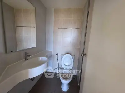 Modern bathroom with sleek fixtures and neutral tiles, featuring a stylish curved sink and toilet.