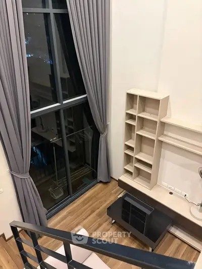 Modern loft apartment with high ceilings and large windows, featuring elegant curtains and stylish shelving.