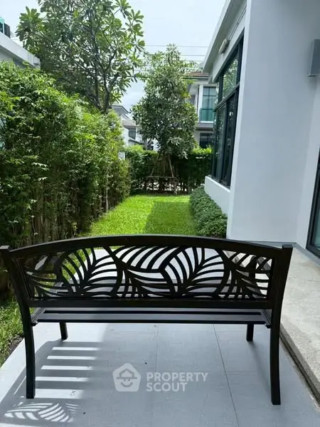 Charming garden view with elegant bench and lush greenery in modern residential setting.