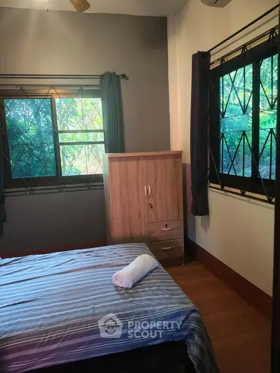 Cozy bedroom with natural light and garden view, featuring a comfortable bed and wooden wardrobe.