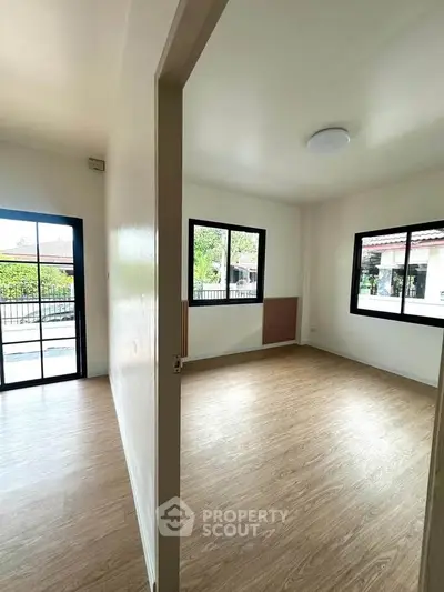 Bright and airy room with large windows and wooden flooring, perfect for a cozy living space.