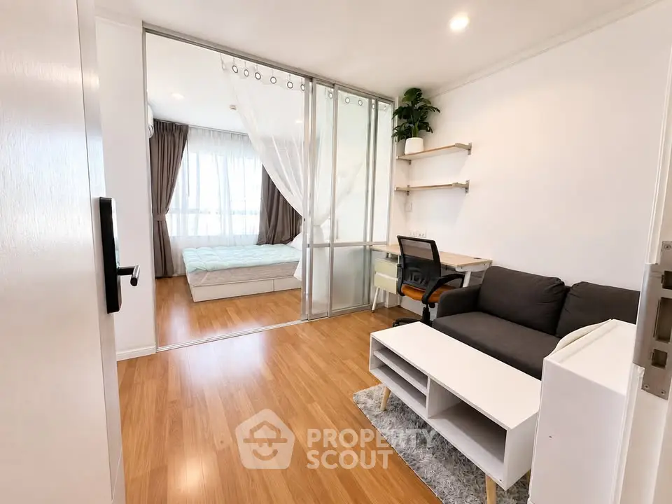 Modern studio apartment with open layout, featuring a cozy living area and a bright bedroom separated by glass doors.