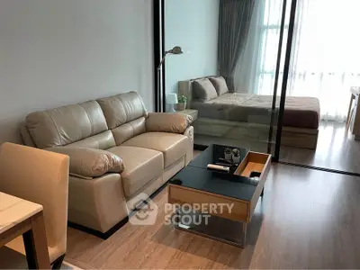 Modern living room with leather sofa and glass partition leading to cozy bedroom.