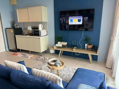 Modern living room with stylish furniture and entertainment setup, featuring a cozy blue sofa and compact kitchenette.