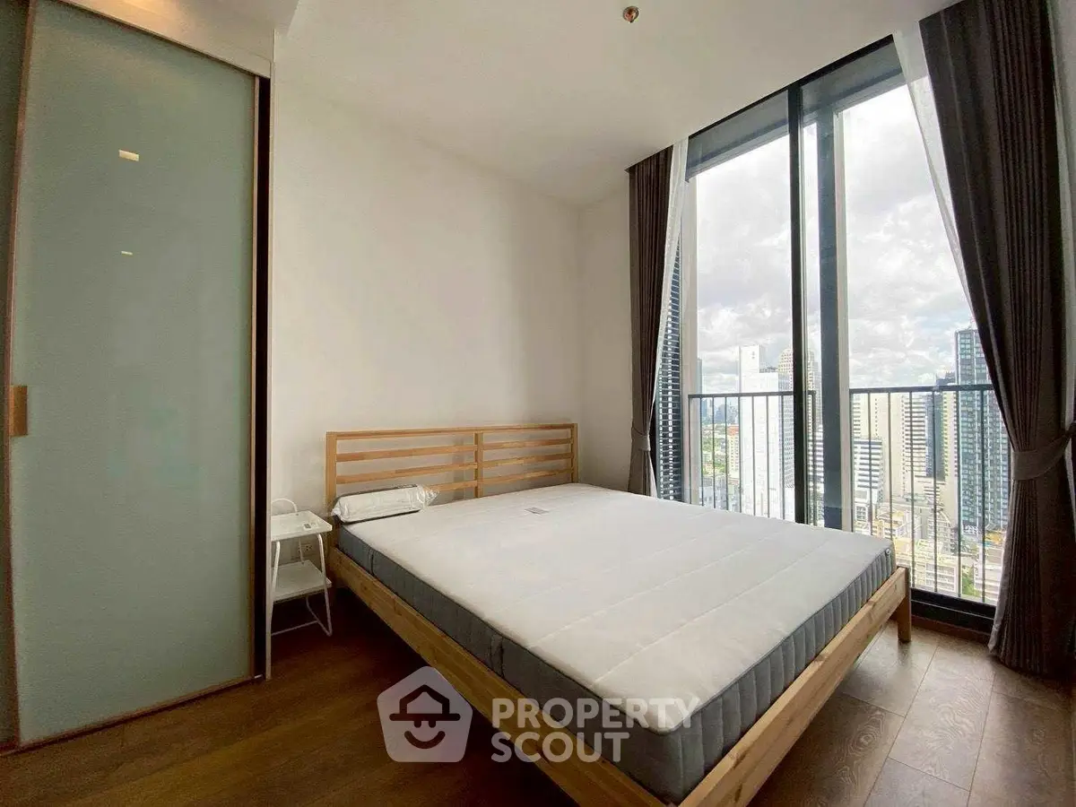 Modern bedroom with city view and large windows in high-rise apartment.