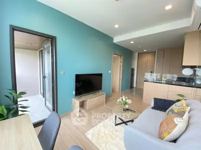 Modern living room with open kitchen and balcony access, featuring stylish decor and natural light.