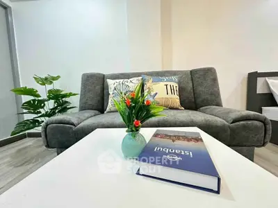 Modern living room with stylish gray sofa and decorative pillows, featuring a coffee table with a book and vase.