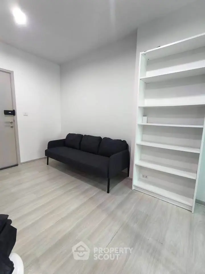 Modern minimalist living room with sleek black sofa and white shelving unit.