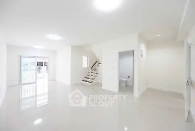 Spacious modern living room with glossy tiled floors and staircase, ideal for family gatherings.