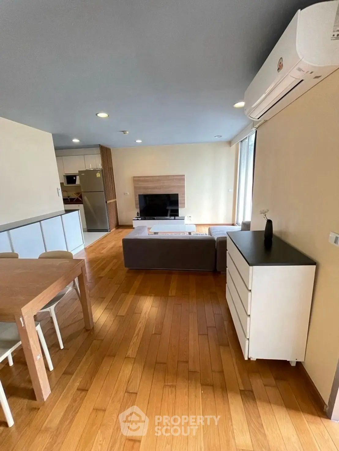 Spacious living room with modern decor and wooden flooring, featuring a cozy dining area and sleek air conditioning unit.