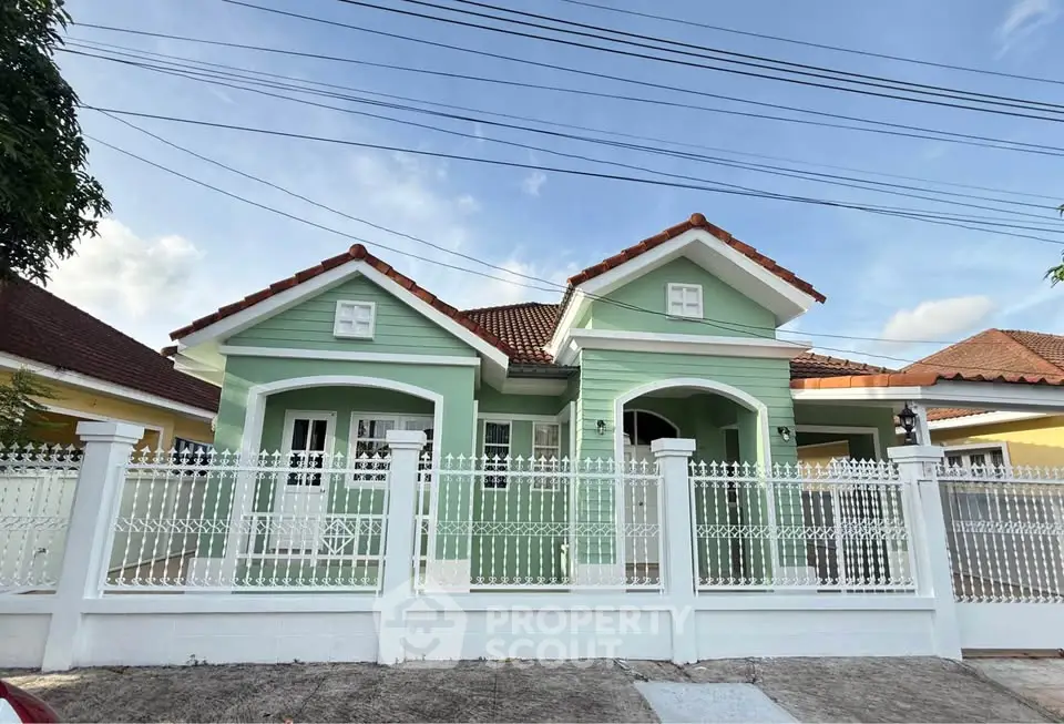 Charming green house with white fence and twin gables in a serene neighborhood.
