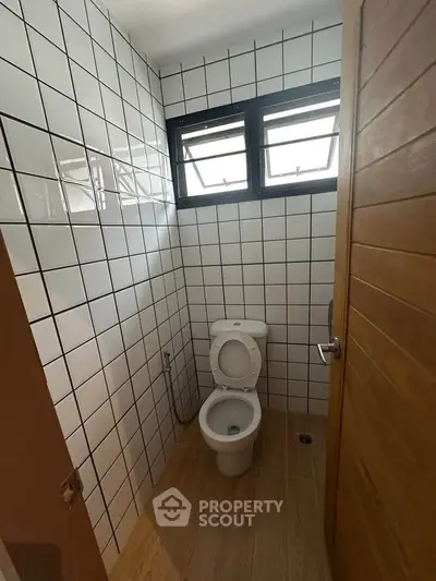 Compact bathroom with tiled walls and wooden door, featuring a modern toilet.
